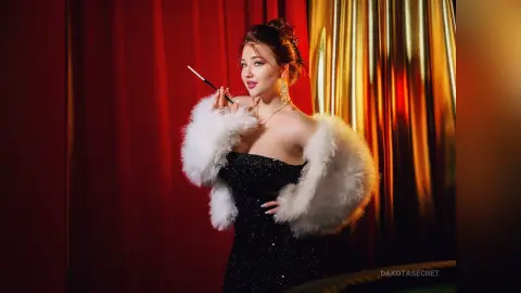 Glamorous woman in a black sequin dress and white faux fur stole posing against red and gold curtains.