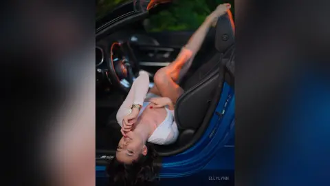 Stylish woman in a white top relaxing in a luxury blue convertible car during a sunset drive.