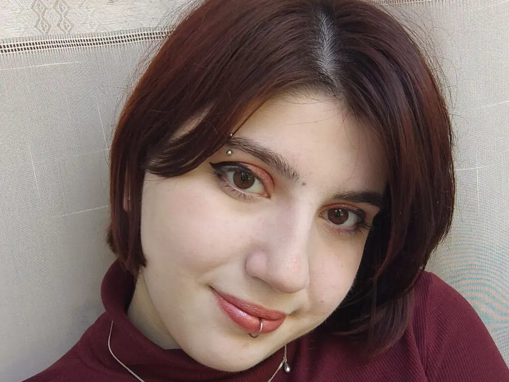 Smiling young woman with short reddish-brown hair and lip piercing wearing a maroon turtleneck sweater.