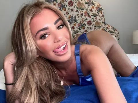 Smiling blonde woman in a blue satin camisole relaxing on a bed in a bright bedroom.