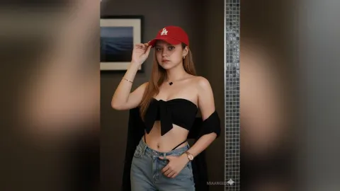 MiaAngelove — MiaAngelove wears a red LA baseball cap and a black strapless crop top with blue jeans while posing indoors.
