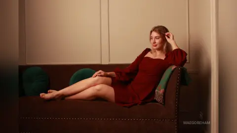 Young woman in a red dress relaxing on a brown sofa in a warm, cozy indoor setting.