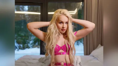 EllieFrosty poses with her hands behind her head, wearing a pink strap bra and matching pink bottoms against a window view of snow.