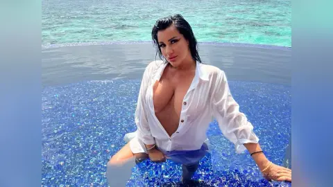 MissyJolie wears an open white button-down shirt while sitting in a blue tiled swimming pool overlooking the ocean.