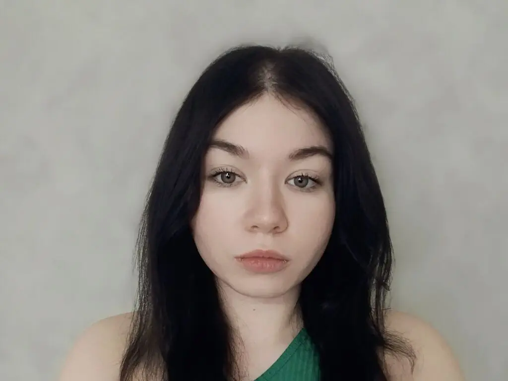 Young woman with long dark hair and natural makeup looking calmly at the camera against a neutral background.