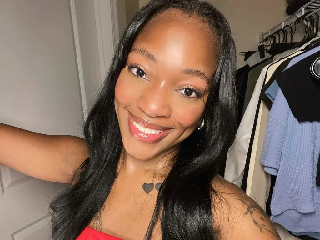 Smiling Black woman with long dark hair wearing a red top in a bright indoor setting.