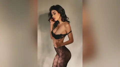 Elegant woman in black lace lingerie and patterned tights posing against a neutral studio background.