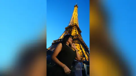 Dolce poses in a black sleeveless top against the lit Eiffel Tower at night.