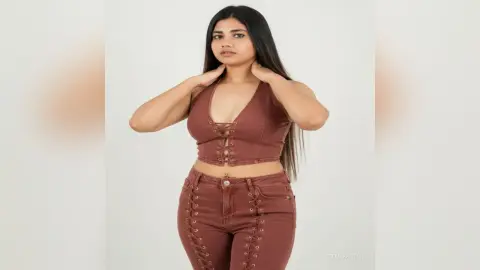 Young woman in a brown lace-up crop top and matching high-waisted trousers posing against a white background.