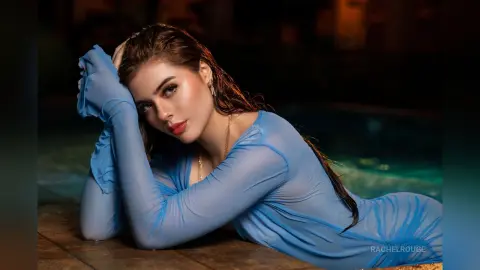 Beautiful woman in a sheer blue long-sleeve top relaxing by a pool at night with a moody atmosphere.