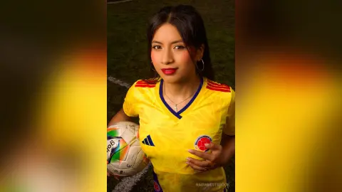 NairaWestbrook wears a yellow soccer jersey while holding a white and green soccer ball against a dark background.