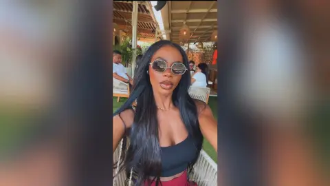 Stylish woman in a black crop top and sunglasses relaxing at an outdoor summer patio lounge.