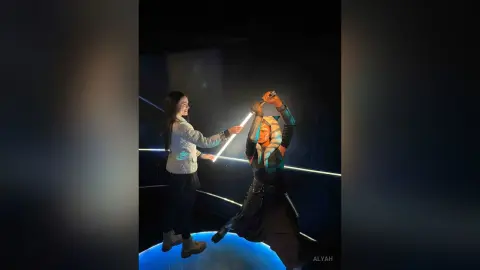 Woman in casual outfit holding a glowing lightsaber in a dark, cinematic sci-fi setting.