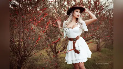 Blonde woman in a white summer dress and brown cowboy hat posing in a dreamy autumn berry field.