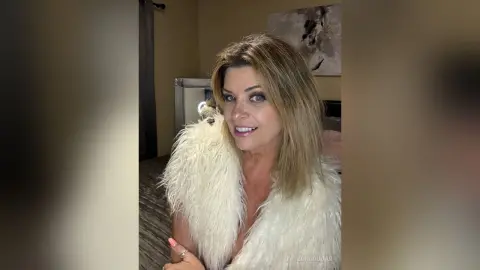 Smiling woman in a cozy white faux fur coat relaxing in a modern living room setting.