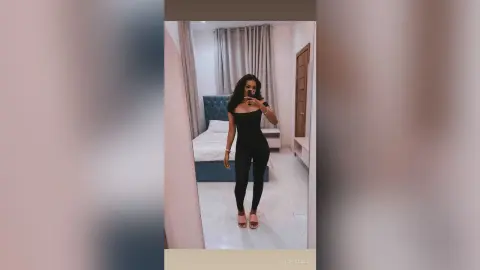Stylish woman in a black jumpsuit posing in a modern bedroom mirror for a chic lifestyle look.