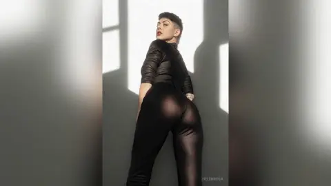 Confident woman in a black long-sleeve bodysuit posing in a bright, minimalist studio setting.