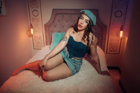 Young woman in denim crop top and shorts relaxing on a cozy bed in warm, moody lighting.