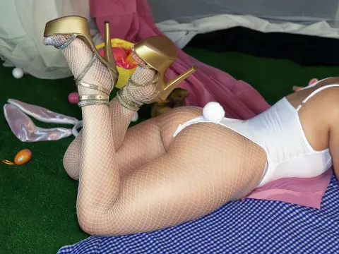 Woman in white lingerie and fishnet tights wearing gold high heels lying on green grass.