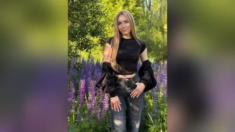 AmiliRay — AmiliRay stands in a field of purple flowers wearing a black crop top and blue jeans.