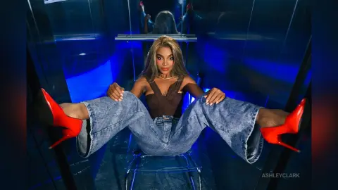 Stylish woman in denim jeans and red high heels sitting in a blue neon lit modern room.