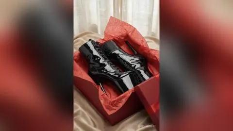 AlienaMoore — AlienaMoore displays a pair of shiny black patent leather high-heeled boots inside a red gift box.