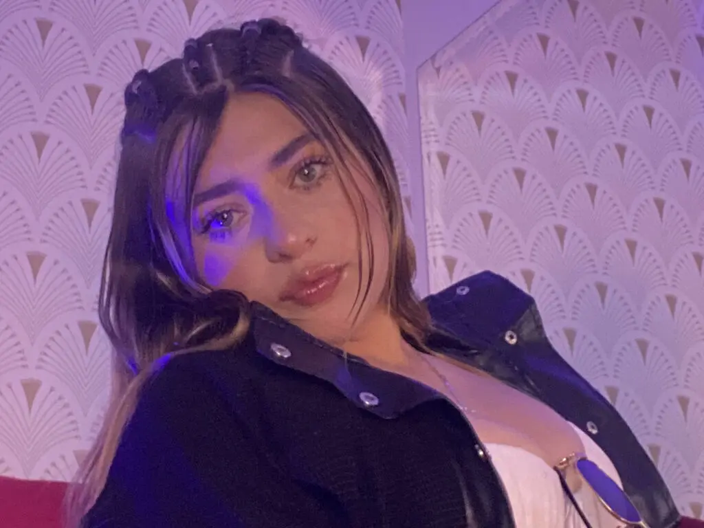 Young woman with long hair in a black jacket posing under moody purple lighting in a patterned room.
