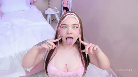Playful young woman with pink hair and lace pink lingerie posing in a bright bedroom.