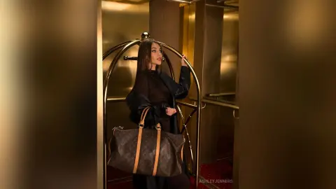 Elegant woman in a black outfit holding a large designer tote bag in a luxurious gold hotel lobby.