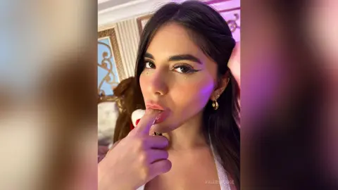 ValeryRouge licks her finger near her lips while looking into the camera with long dark hair and winged eyeliner.