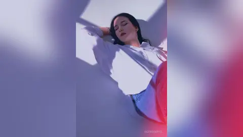 Young woman in a white button-down shirt lying in soft sunlight for a dreamy, aesthetic portrait.