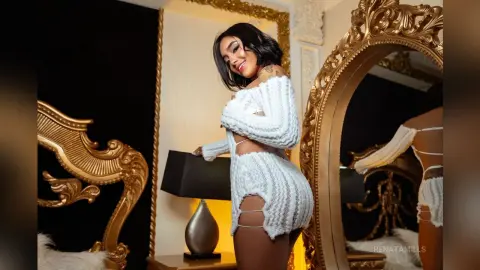 Smiling woman in a white knit co-ord set posing in a luxurious gold decor bedroom setting.