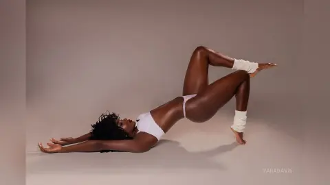 Athletic Black woman in white minimalist swimwear performing a yoga bridge pose in a studio setting.