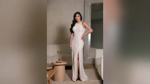 Elegant woman in a white lace halter maxi dress posing in a modern minimalist living room.