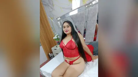 Beautiful woman in red lace lingerie sitting on a white bed in a bright, modern bedroom.