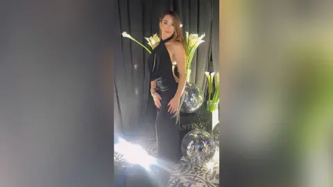 KimRece stands in a black cut-out dress against a dark backdrop with disco balls and white flowers.
