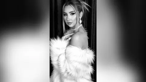 Elegant woman in white faux fur coat and pearl necklace posing for a glamorous black and white portrait.