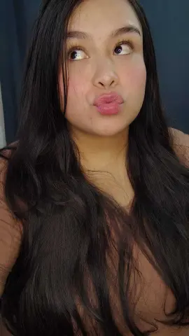 Young woman with long dark hair making a playful pouty face in a casual indoor setting.