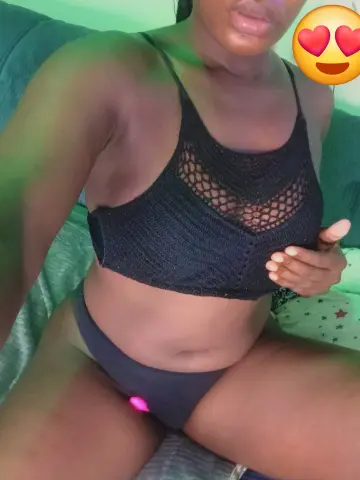 Woman in black crochet bralette and bikini bottoms relaxing on a green sofa in soft lighting.