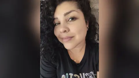 Smiling woman with curly dark hair wearing a black t-shirt in a bright indoor setting.