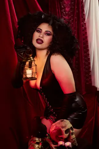 Glamorous woman in black gothic corset and gloves holding a vintage lantern against red velvet curtains.