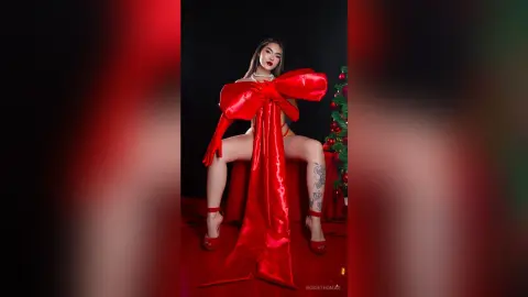 Glamorous woman in a dramatic red satin bow outfit posing in a festive holiday setting.