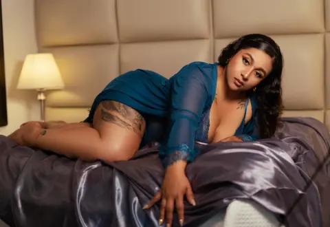 Beautiful woman in a blue lace negligee lounging on a bed in a moody, intimate bedroom setting.