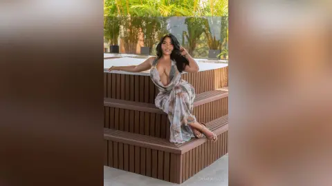 DayanaHille sits on the edge of a white hot tub wearing a sheer, patterned white wrap dress.