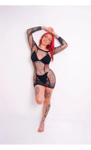 Red-haired woman in a black sheer mesh mini dress posing against a white background with a confident mood.