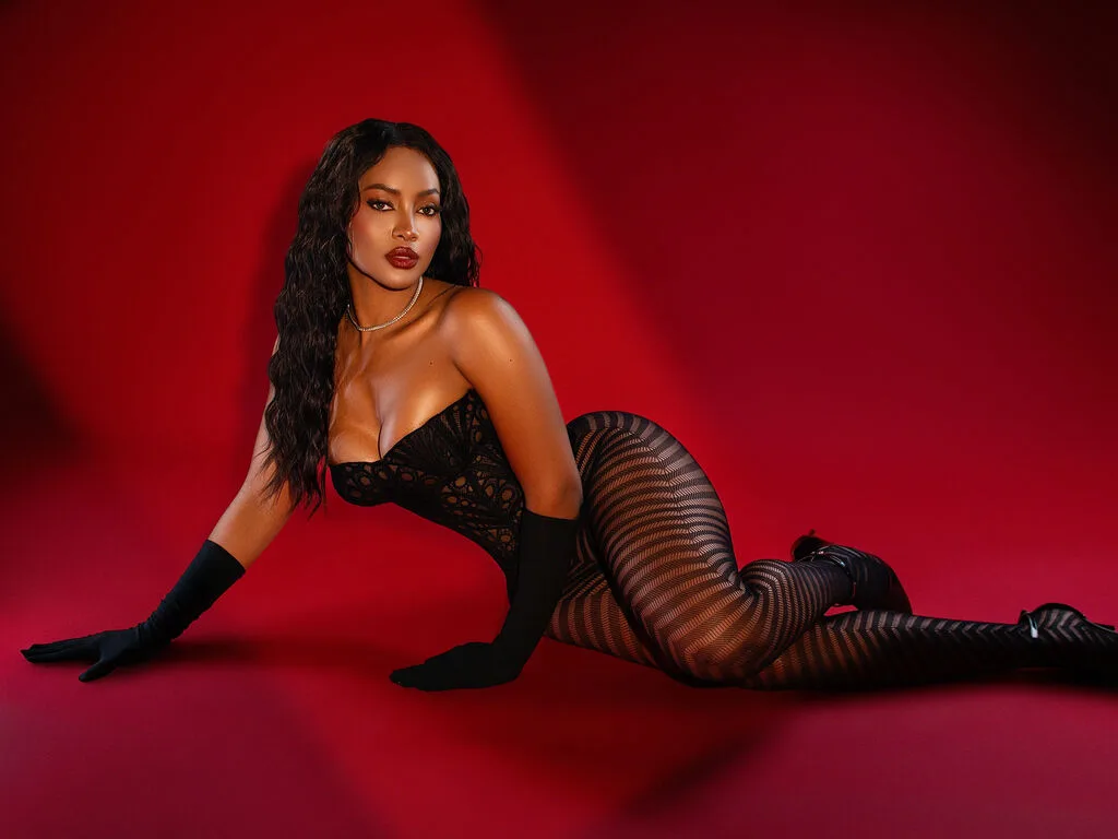 NohomiCambel poses on a red background wearing a black lace bodysuit and long black gloves.