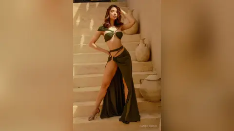 Elegant woman in an olive green cut-out maxi dress posing on stone stairs in warm sunlight.