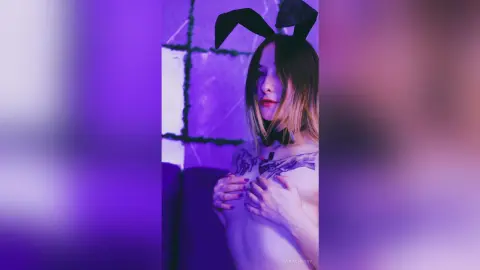 Young woman in bunny ears and black choker posing in moody purple lighting.
