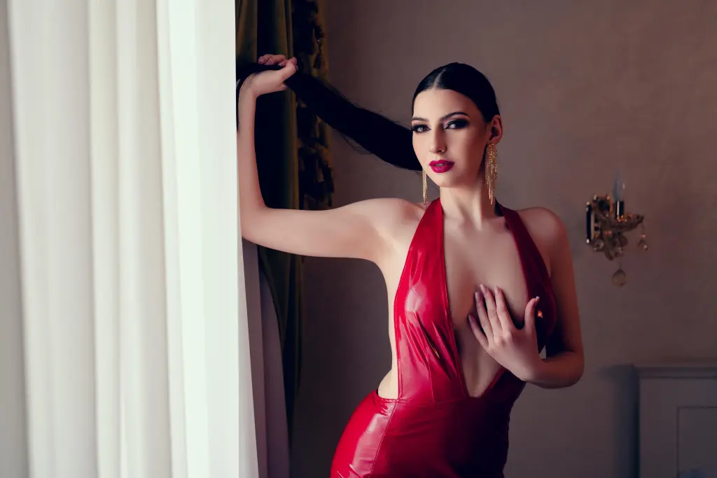 Elegant woman in a black latex outfit posing against a dramatic red glowing background with a moody atmosphere.