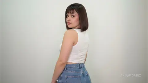 Young woman with brown bob hair wearing a white tank top and blue jeans against a plain white background.
